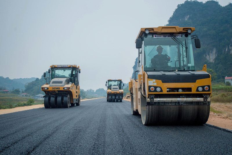 Đến khi sáng tỏ, điều kiện thời tiết thuận lợi hơn, nhịp độ thi công được đẩy nhanh. Trên mặt đường, dây chuyền thảm bê tông nhựa vận hành liên tục